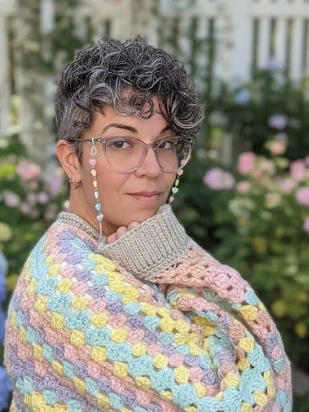 Natalie in a pastel granny-stripe crochet cardigan in a flower garden